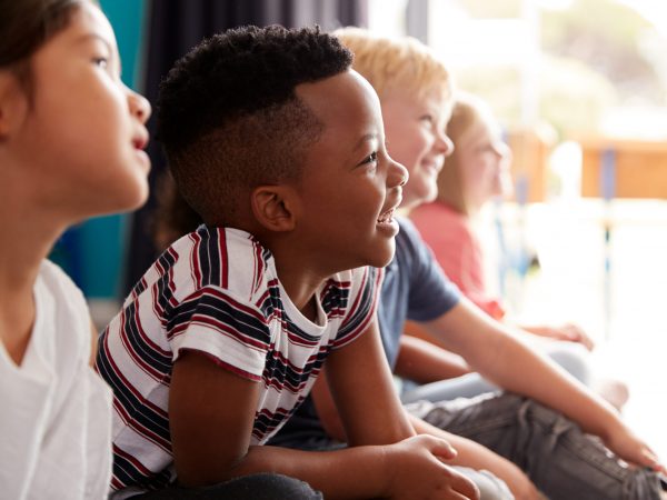 Group Of Elementary School Pupils Sitting On Floor Listening To Teacher